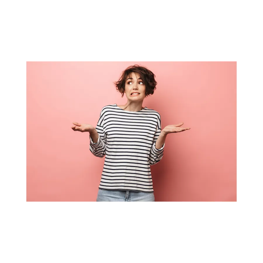 A female with short brown hair in a stripped black and white shirt. Standing in front of a pink background with her hands up looking confused. 
